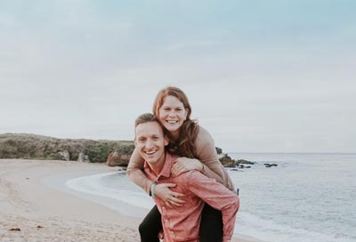 A man piggybacking a Russian woman at the beach.